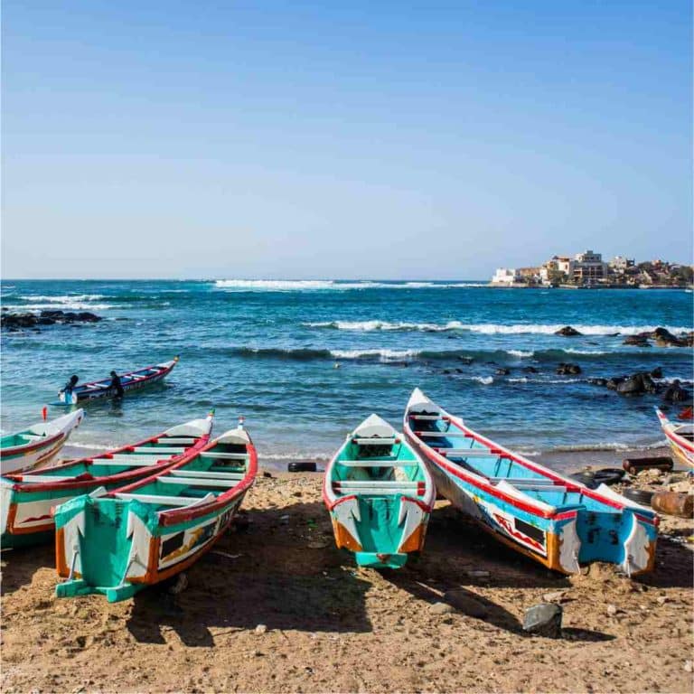 3 green and blue colourful West African fishing boats on the beach with the sea in the background in Senegal