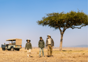 Father and two children walking away from the safari truck, with an acacia tree in the background.