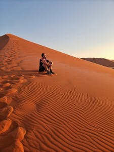 A man enjoys solitude while sitting on a sand dune in the Namib Desert during sunset.