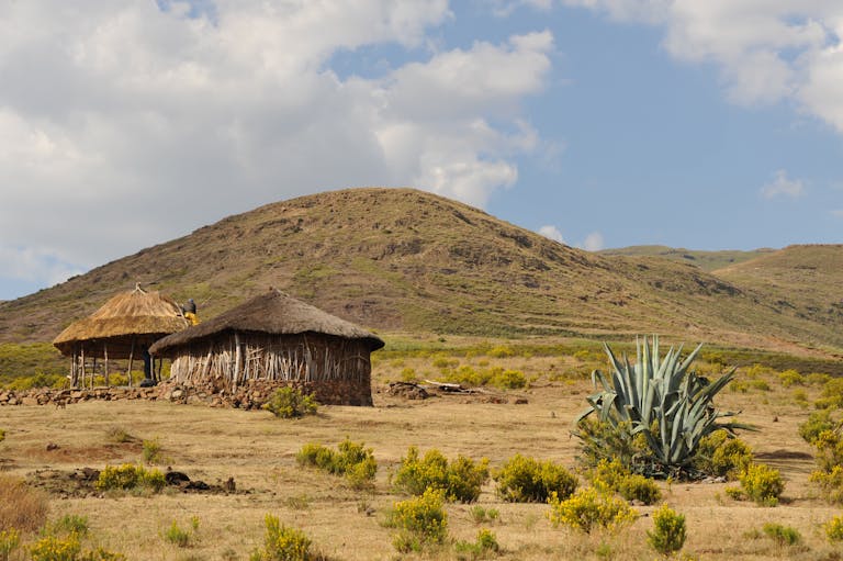 19 Day South Africa, Lesotho and Eswatini Group Tour 6 Scenic view of traditional huts in a dry, mountainous African landscape under a blue sky.