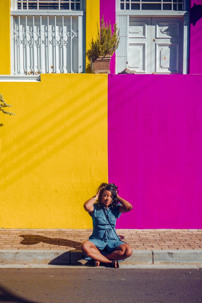 Home 6 A woman poses against a vibrant yellow and pink wall, creating a striking urban portrait with bold colors.